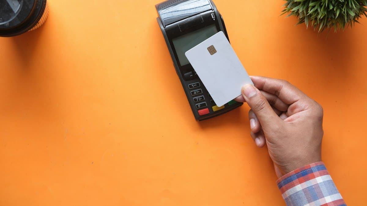 A hand holding a card next to a payment terminal on an orange background